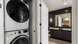 A laundry area with stacked washers and dryers, a modern bathroom with a dark countertop and a large mirror. - Top Floor Downtown Lux Condo Rainey * Rooftop Pool (Austin)