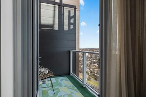 Un balcón con vista a una zona residencial, una silla y un tapete estampado.