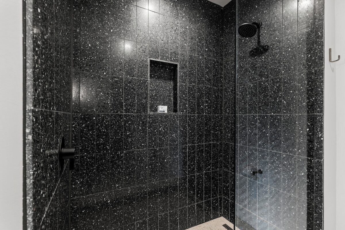 A shower with a handheld showerhead, a wall-mounted control panel, and a rectangular mirror.