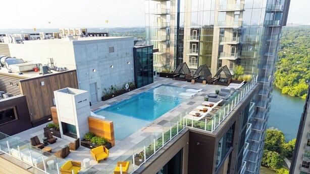 A rooftop pool with glass railings, outdoor seating, and a view of a river and surrounding buildings. - Rooftop Riverside Condo | *Rainey St*, Local Attractions, Rooftop Pool! (Austin)