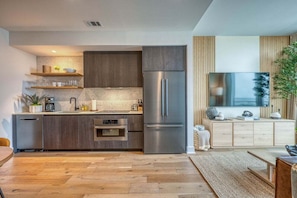A modern kitchen with built-in appliances, wooden cabinets, and a flat-screen TV. - Rooftop Riverside Condo | *Rainey St*, Local Attractions, Rooftop Pool! (Austin)