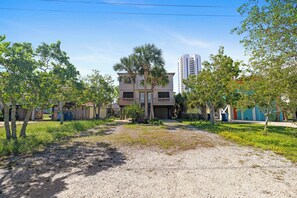 A residential area with a two-story building, a gravel driveway, and surrounding greenery. - 3 Palms Duplex by Liquid Life (Gulf Shores)