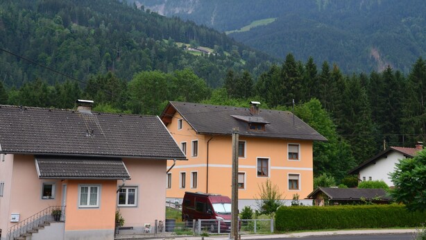 A residential area with houses, a red van, and a mountainous backdrop.