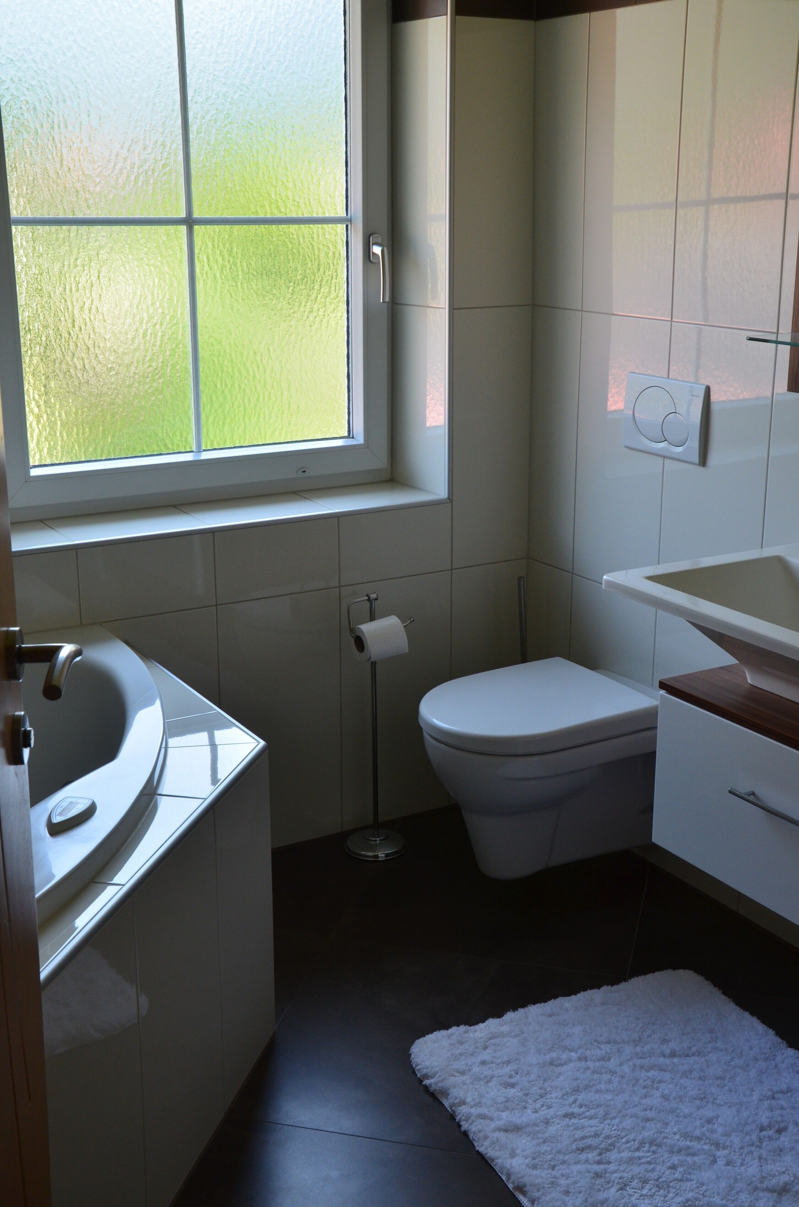 A bathroom with a white sink, toilet, and a window with frosted glass.