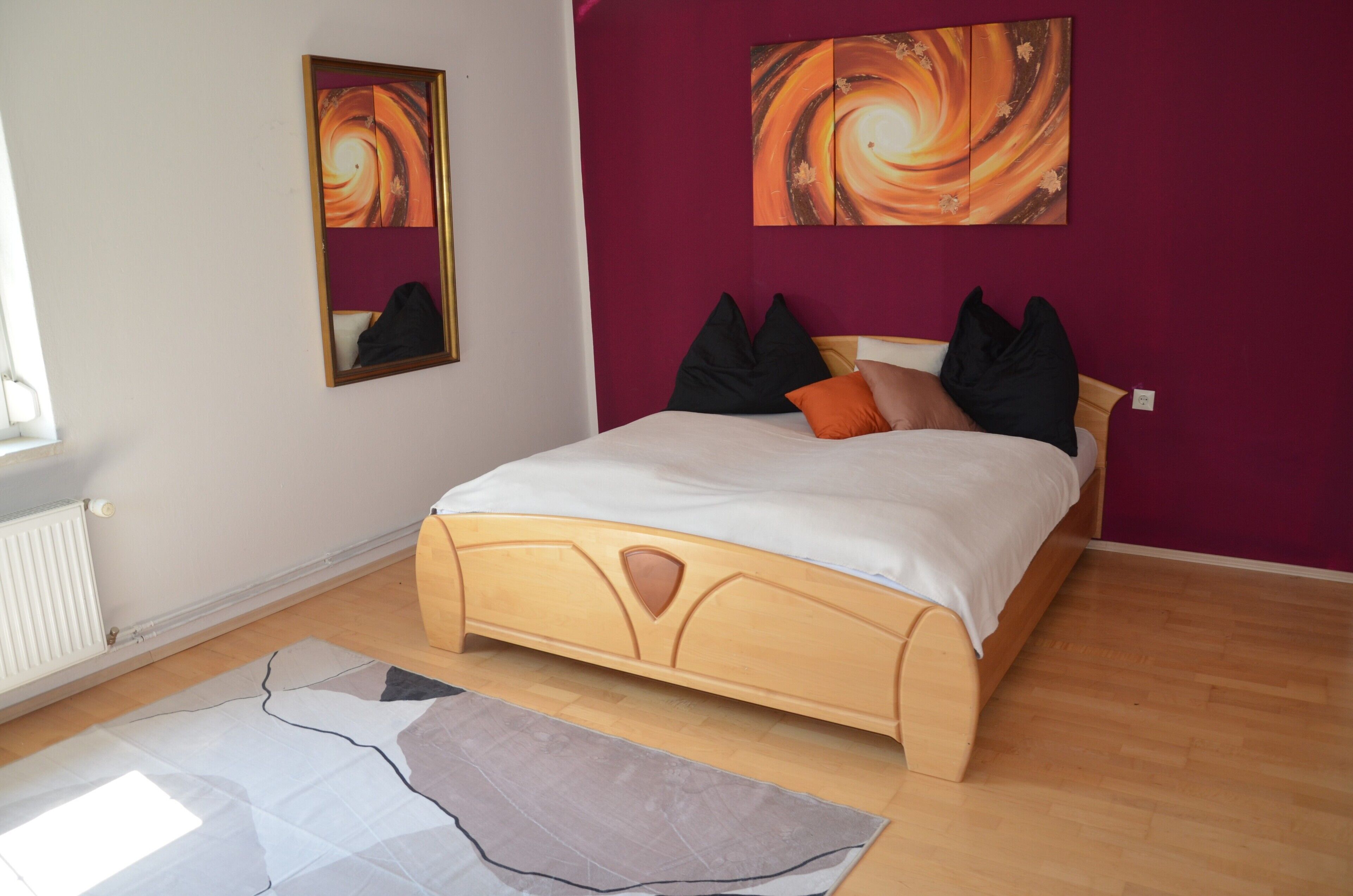 A bedroom with a bed, a radiator, a window, and two wall-mounted artworks.