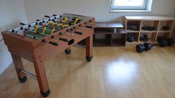 A wooden foosball table in a room with a window, shelves with weights, and a bench.