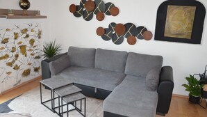 A modern living room with a grey sectional sofa, a small coffee table, decorative wall art, and a potted plant.