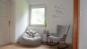 A room with a white door, a window with a view of greenery, a grey bean bag chair, a grey rocking chair, and a wall with inspirational text.