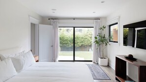 A bedroom with a bed, a TV, a potted plant, and a sliding glass door to a garden. - Luxe Venice Oasis | Abbot Kinney | Beach (Venice)