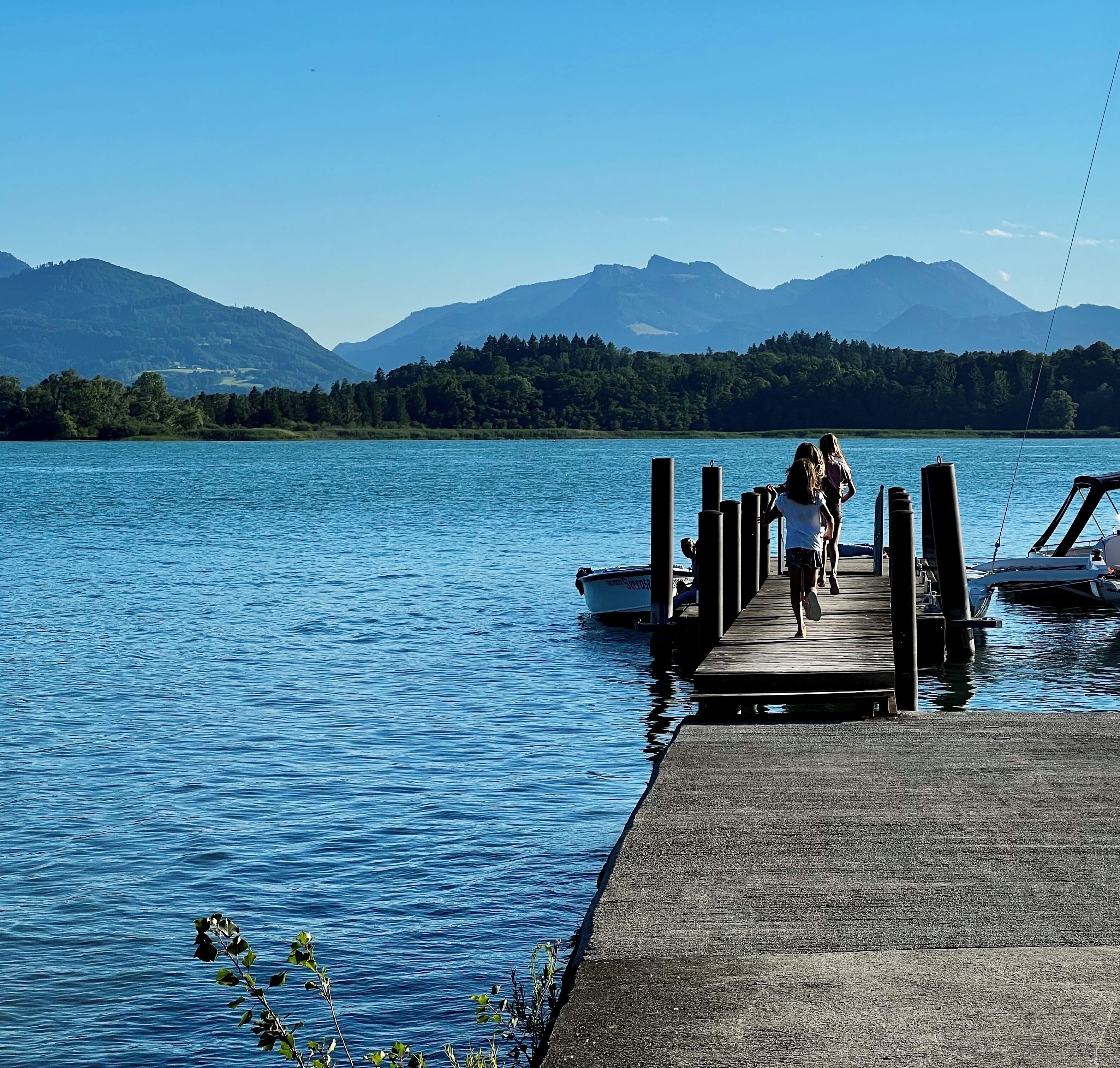 Un muelle de madera que se adentra en un lago, con montañas al fondo.