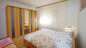 A bedroom with a bed, a wardrobe, a bedside table, and a window with curtains. - Holiday apartment Zoa (Pula)