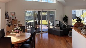 Un vaste espace de vie avec une grande porte-fenêtre coulissante donnant sur un patio extérieur, un ventilateur de plafond et une table à manger en bois avec des chaises.