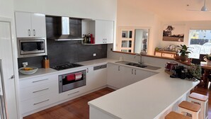 Une cuisine moderne avec des meubles blancs, un four encastré, un micro-ondes, un évier et un grand îlot central doté de tabourets de bar.