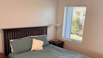 A bedroom with a bed, a nightstand, a lamp, a ceiling fan, and a window with blinds.