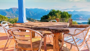 Una mesa de madera con sillas de metal, una pared de piedra y vistas a montañas y un lago.