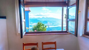 Una habitación con una mesa y sillas, una ventana que ofrece vistas a las montañas y un jarrón con flores sobre la mesa.