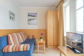 A room with a sofa, a small table with a plant, a TV on a stand, and a wardrobe. - Charmante Ferienwohnung im Seepark Sellin mit Ahoi-rabatt (Sellin)
