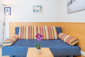 Ein blaues Sofa mit gemusterten Kissen, ein kleiner Tisch mit einer Topfpflanze und Bilder an der Wand.
