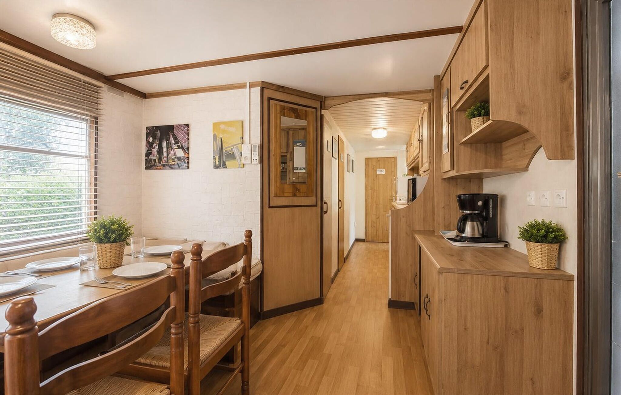 A compact kitchen with wooden cabinets, a dining table with chairs, and a coffee maker.