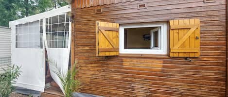 Una cabaña de madera con ventana y contraventanas, una puerta y un pequeño porche.