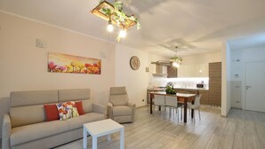En moderne stue med sofa, lænestol, spisebord og et køkken i baggrunden.