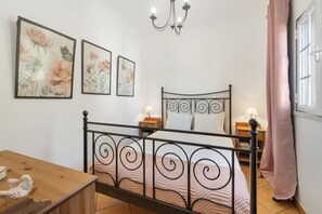 Une chambre à coucher avec un lit en métal, une table de chevet en bois, une commode et une fenêtre avec des rideaux.