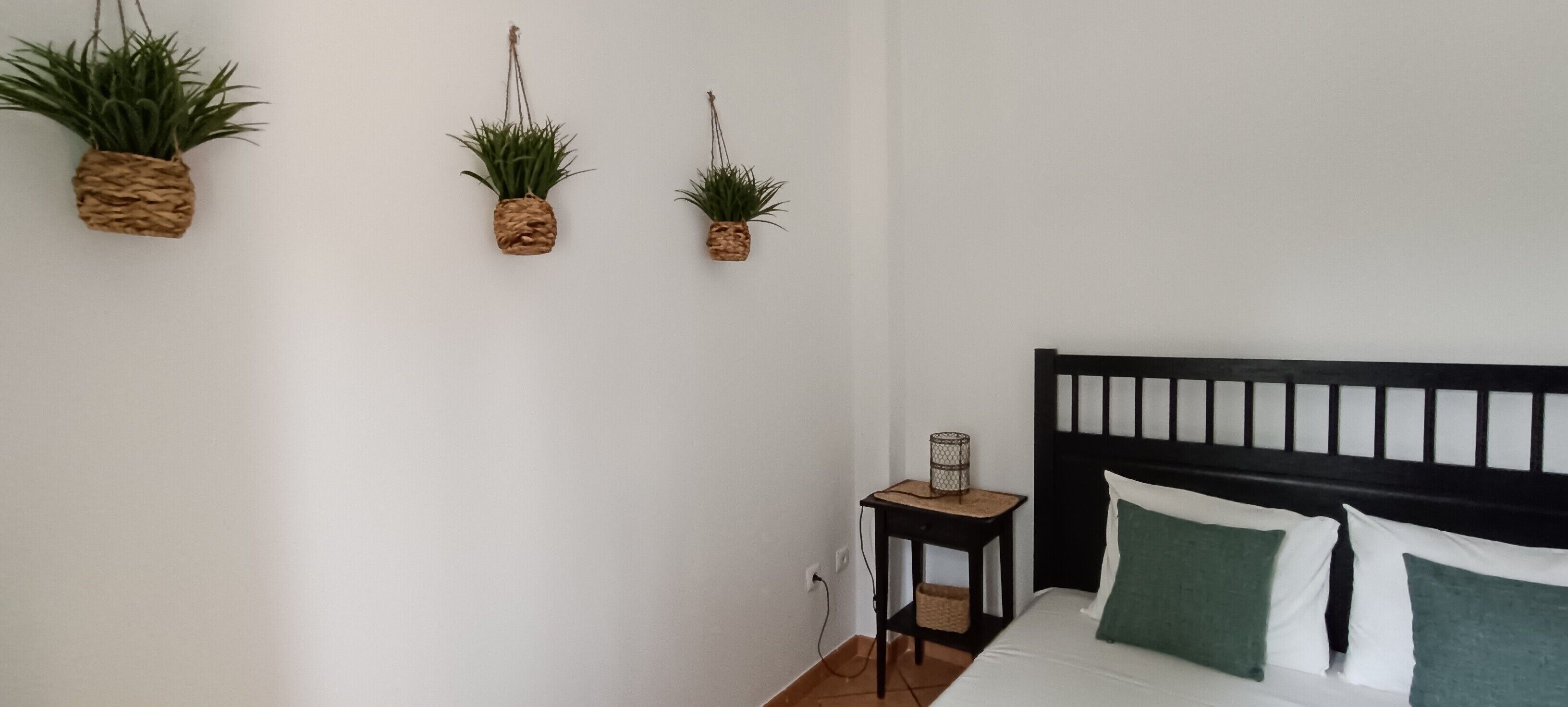 Een slaapkamer met een bed, een nachtkastje en drie wandplanters.