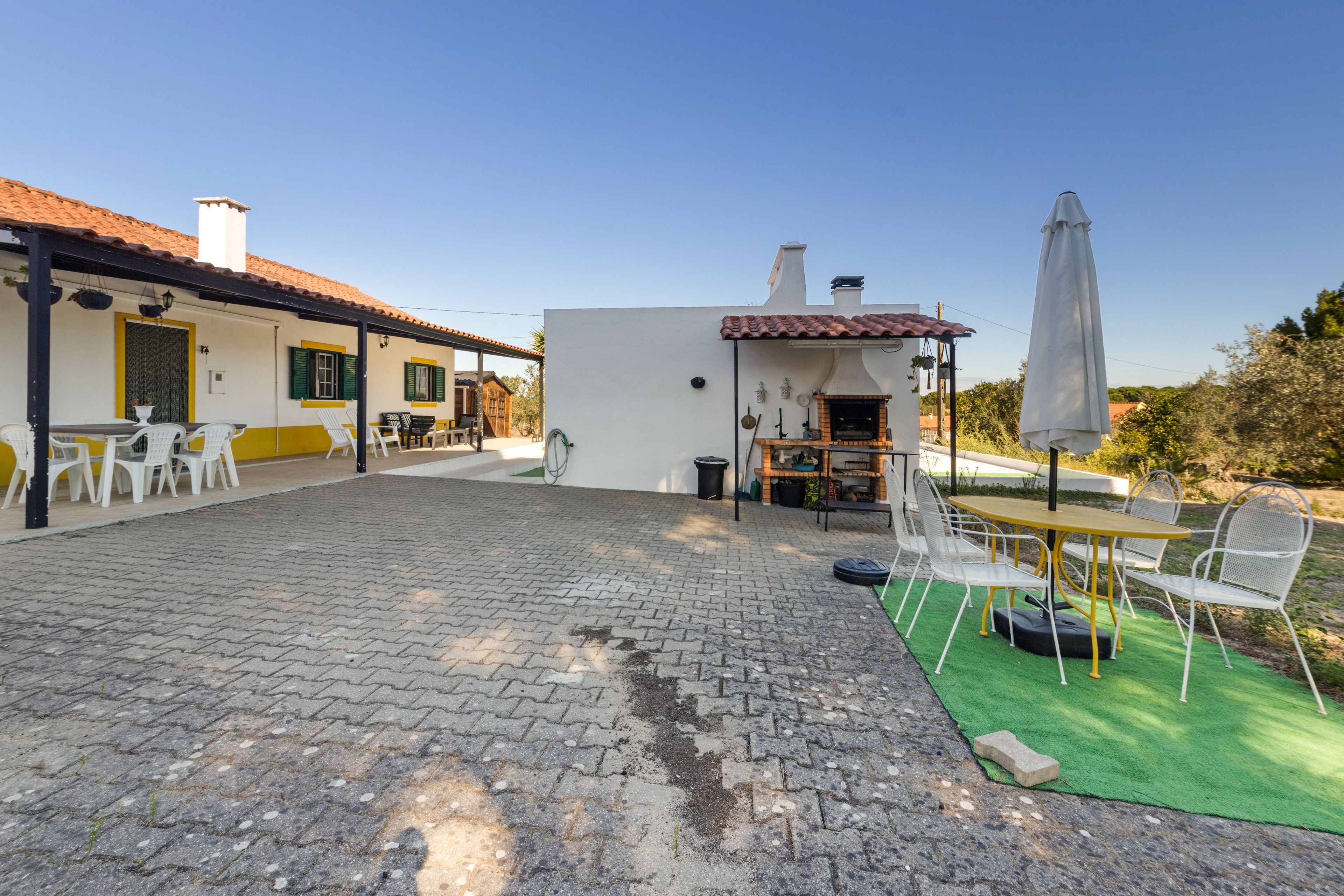 Un patio con suelo empedrado, zona de estar al aire libre con sillas y mesas, una parrilla y un porche cubierto.