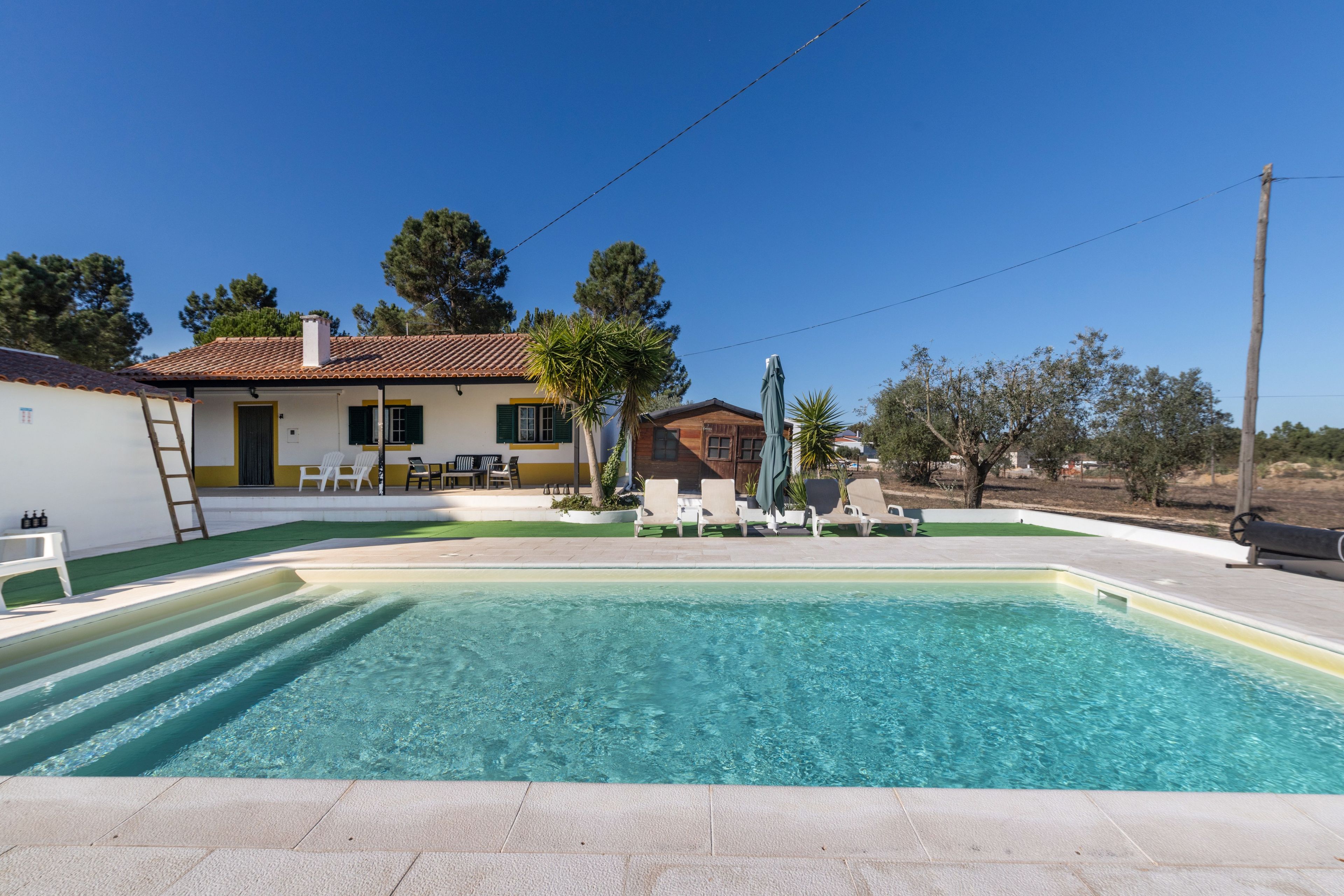 A swimming pool with clear water, surrounded by a patio with lounge chairs and a table.