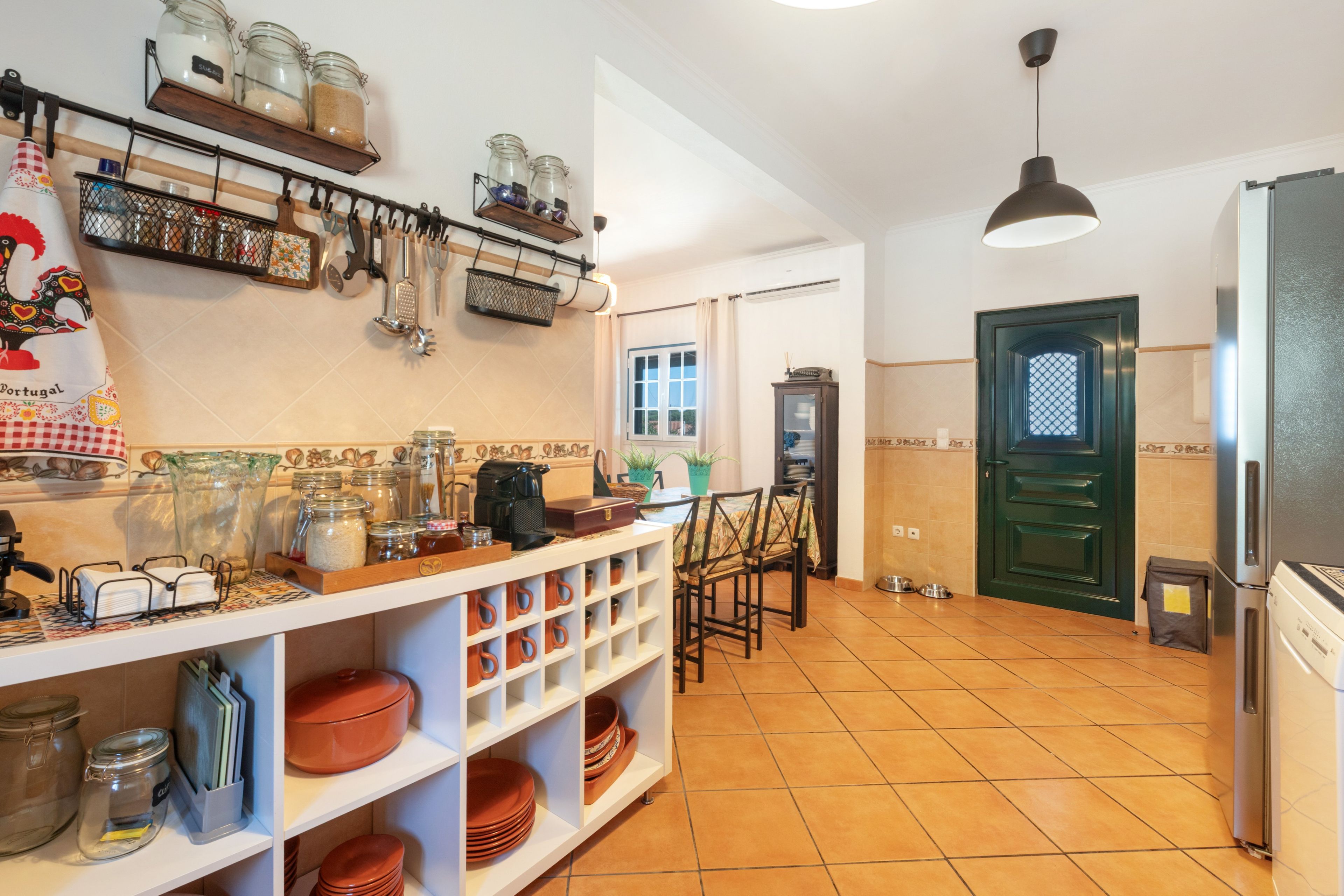 Una cocina con estantes que sostienen frascos, una cafetera y un comedor con sillas y una mesa.