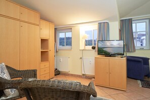 A compact living space with a television, wicker furniture, a radiator, and a view of the outside. - Geraumige Ferienwohnung im Seepark Sellin mit Wlan (Sellin)