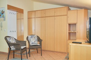Ein Zimmer mit zwei Korbstühlen, einem Holzschrank, einem Fernseher auf einer Holzkommode und einem Kalender an der Wand.