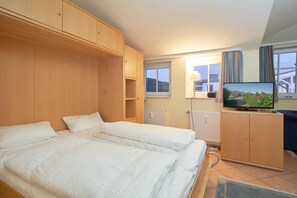 A bedroom with two beds, a television, wooden cabinets, and a view of the outside. - Geraumige Ferienwohnung im Seepark Sellin mit Wlan (Sellin)