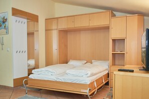 Ein gemütliches Schlafzimmer mit Bett, Kleiderschrank, Fernseher und einem kleinen Schreibtisch.