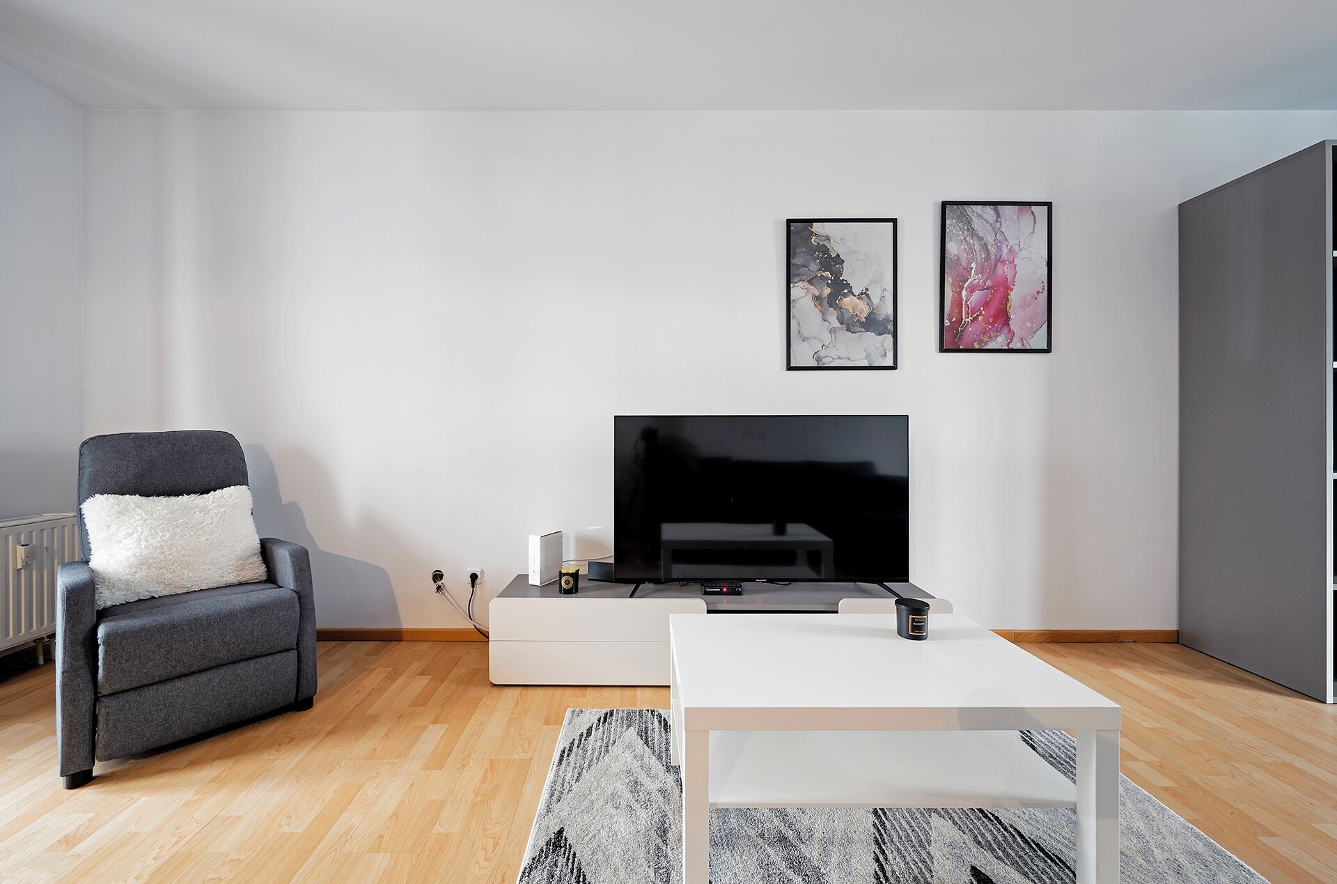 Ein modernes Wohnzimmer mit grauem Sofa, weißem Couchtisch, Flachbildfernseher und abstrakten Wandbildern.