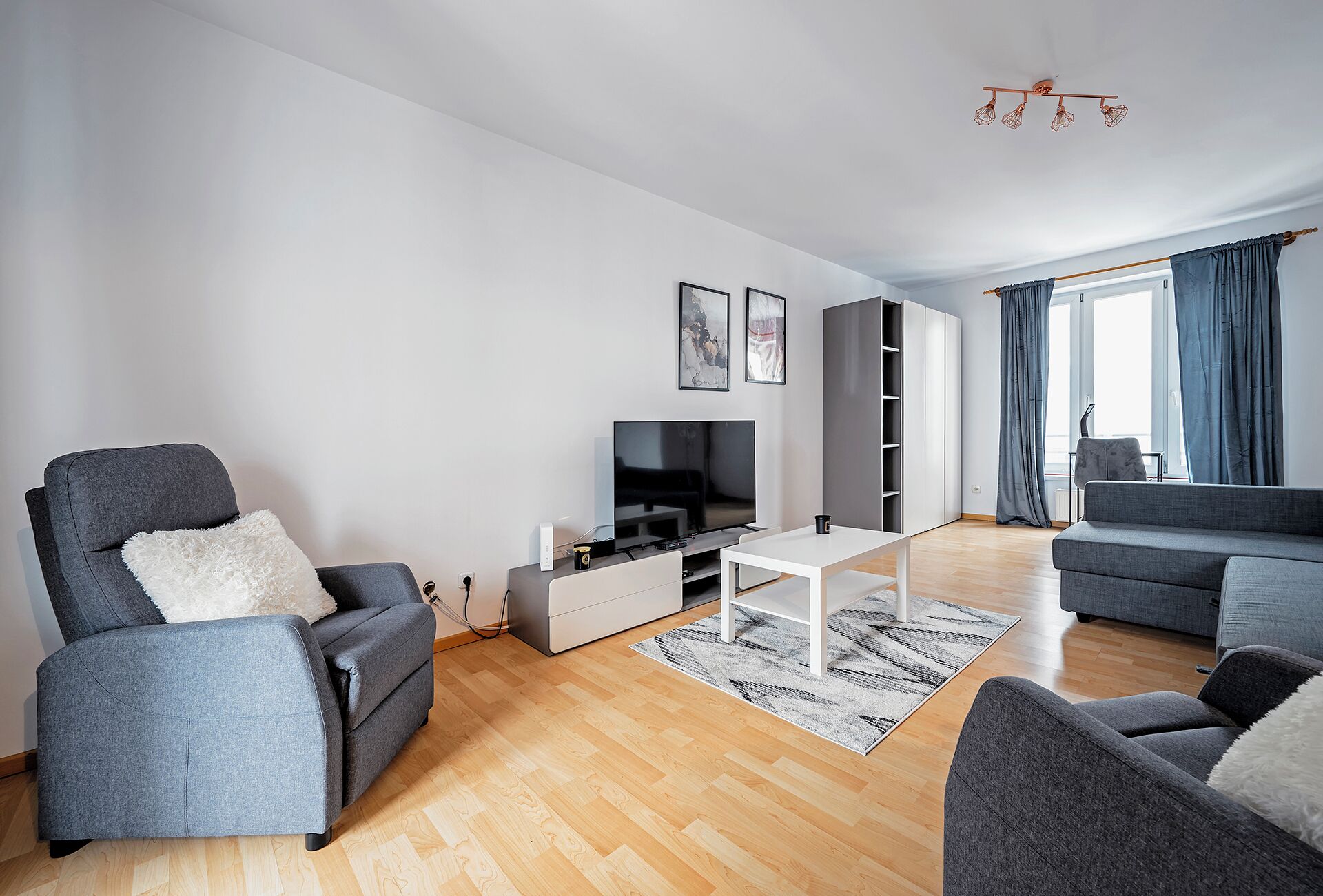 A modern living room with a grey sofa, a white coffee table, and a flat-screen TV.