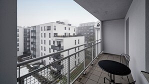 Uma varanda com grades de metal, uma mesa pequena e cadeiras.