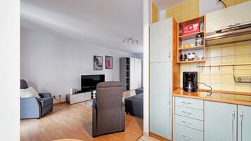 Un espacio habitable pequeño con sofá, televisión, kitchenette y zona de comedor.