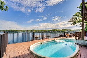 Eine Holzterrasse mit Whirlpool und Gartenmöbeln mit Blick auf einen See.