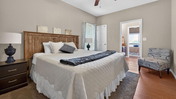 Quarto com cama, ventoinha no teto, mesa de cabeceira, cadeira e porta que dá para outro cômodo.