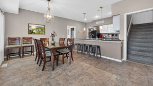 Uma sala de jantar com mesa e cadeiras de madeira, uma cozinha com balcão e uma escada.