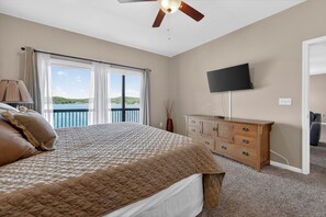 A bedroom with a bed, a dresser, a television, and a view of the sea. - Lakefront Ozarks Home: Pool, Deck, View, Sleeps 26 (Camdenton)