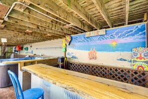 Uma área de bar com teto de madeira, um mural de uma cena de praia e uma decoração com cabeça de tiki.