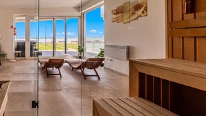 A spacious indoor area with a view of the sea through large glass doors, wooden benches, and a modern ceiling design. - Lelle Marine-hanna Pool Apartment (Balatonlelle)