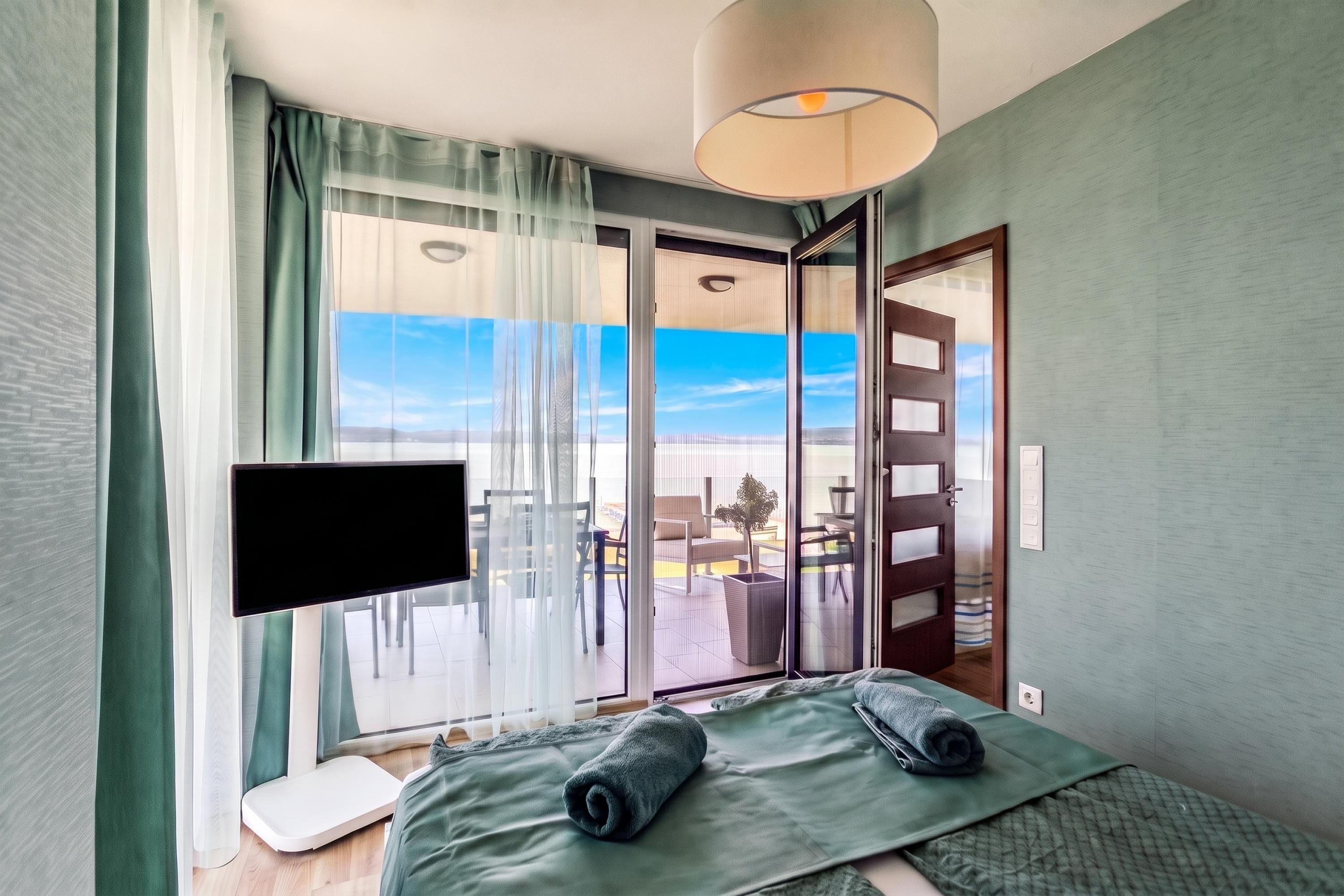 Ein Hotelzimmer mit Bett, Fernseher, einem Fenster mit Vorhängen und Blick ins Freie.