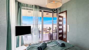 Ein Hotelzimmer mit Bett, Fernseher, einem Fenster mit Vorhängen und Blick ins Freie.
