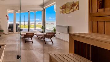 A spacious indoor area with a view of the sea through large glass doors, wooden benches, and a modern ceiling design.