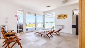 A spacious room with a large sliding glass door leading to an outdoor area, a wooden bench, a small table, and a wall-mounted air conditioning unit. - Lelle Marine-hanna Pool Apartment (Balatonlelle)