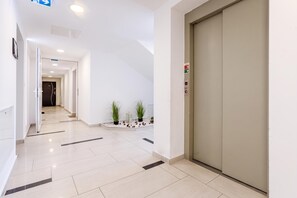 A modern hotel corridor with a closed elevator, a clear path to a room, and a small plant arrangement. - Lelle Marine-hanna Pool Apartment (Balatonlelle)