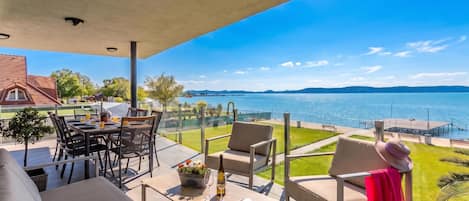 A covered outdoor seating area with a view of a lake and distant hills.